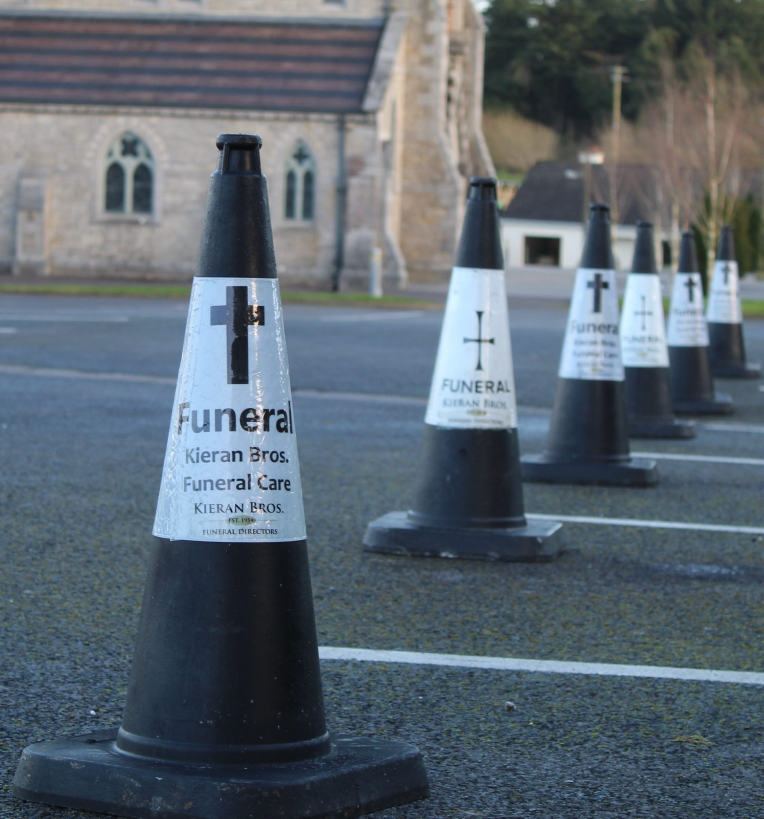 A line of branded funeral traffic cones marking a route outside a church.